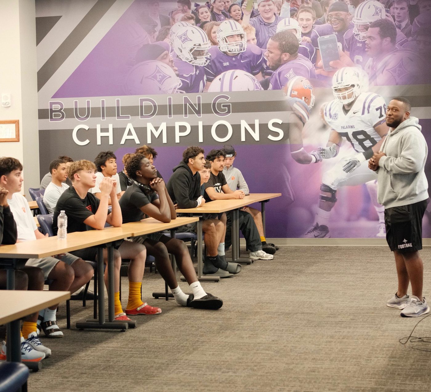 A Furman coach talking recruiting with TOUR athletes in the team meeting room